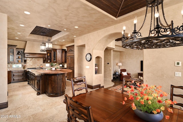 dining area with recessed lighting, a textured wall, arched walkways, a tray ceiling, and a notable chandelier