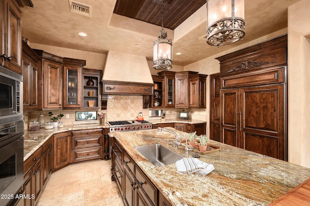 kitchen with a sink, visible vents, custom exhaust hood, a raised ceiling, and appliances with stainless steel finishes