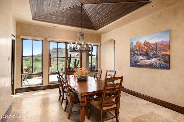 dining space featuring an inviting chandelier, arched walkways, a tray ceiling, wood ceiling, and baseboards