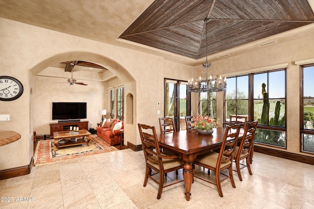 dining area with baseboards, a tray ceiling, ceiling fan with notable chandelier, and arched walkways