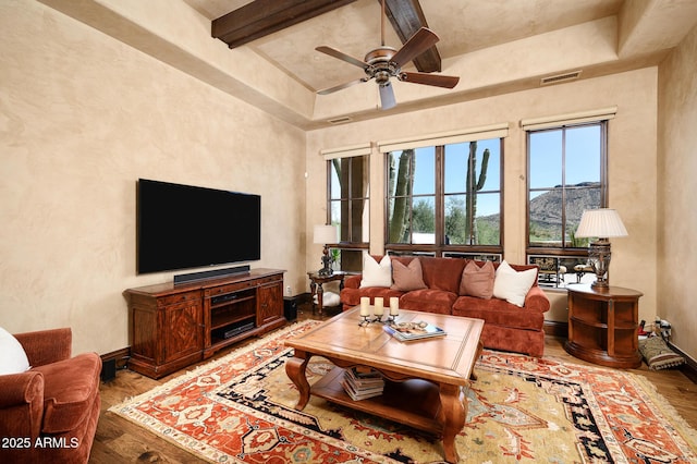 living area with wood finished floors, visible vents, beamed ceiling, a ceiling fan, and baseboards