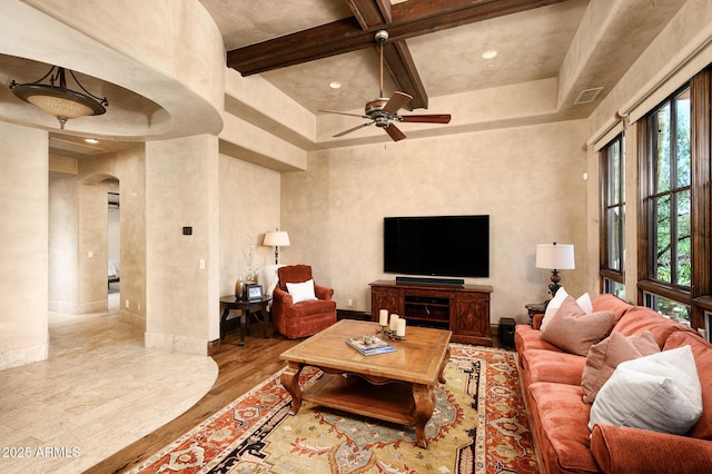 living room featuring baseboards, ceiling fan, wood finished floors, arched walkways, and beam ceiling