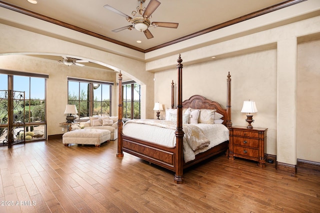 bedroom featuring crown molding, wood finished floors, baseboards, and arched walkways