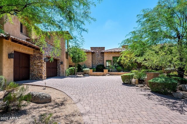 exterior space featuring stone siding, a tile roof, a garage, stucco siding, and decorative driveway