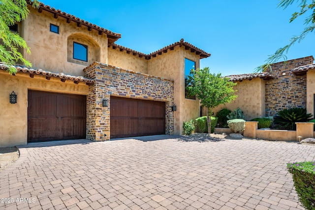 mediterranean / spanish-style house with stone siding, stucco siding, a tile roof, and decorative driveway