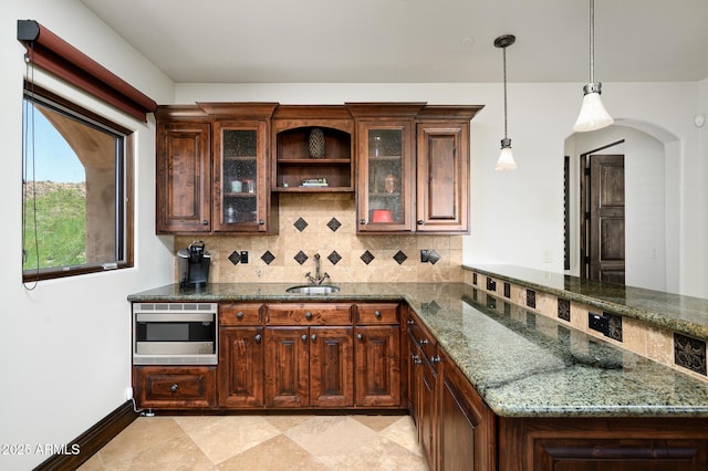 bar featuring hanging light fixtures, a sink, stainless steel microwave, baseboards, and decorative backsplash