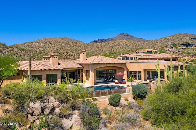 rear view of house with a chimney, a mountain view, a patio, an outdoor pool, and stucco siding