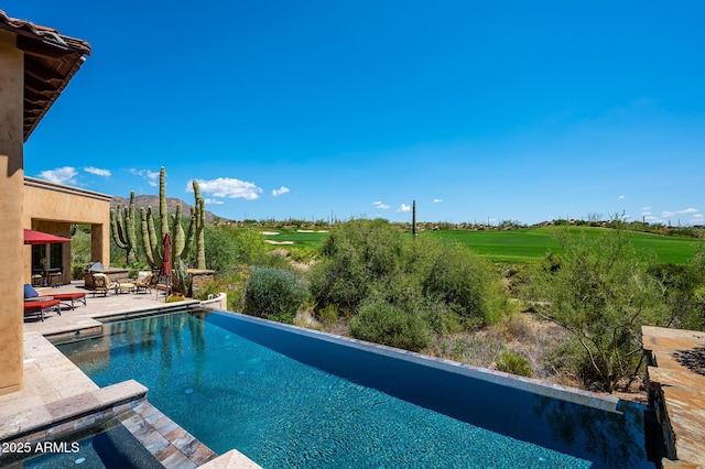view of swimming pool with an infinity pool, a patio, and view of golf course