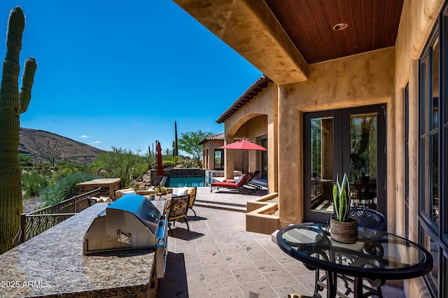 view of patio / terrace featuring an outdoor kitchen, an outdoor pool, a mountain view, and french doors
