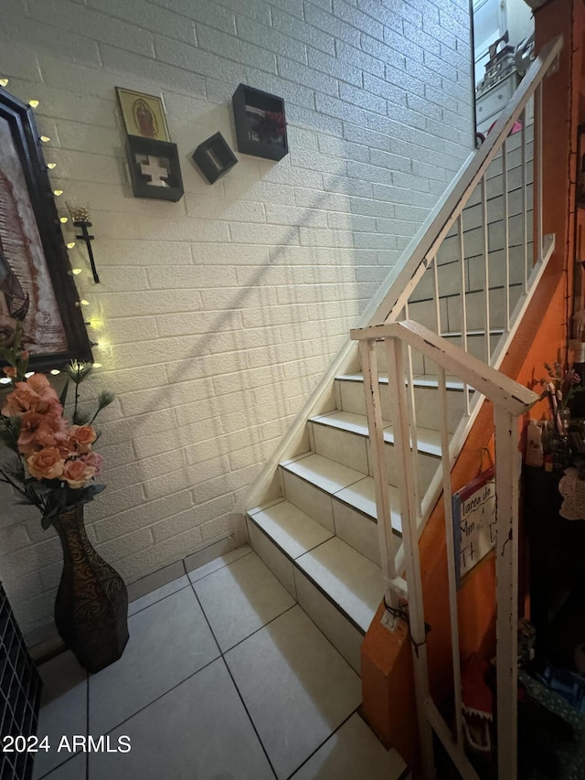 stairway with brick wall and tile patterned floors