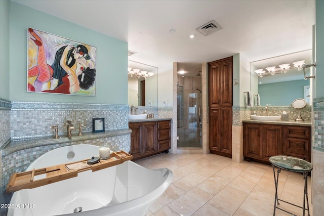 full bath with visible vents, a shower stall, two vanities, a soaking tub, and a sink