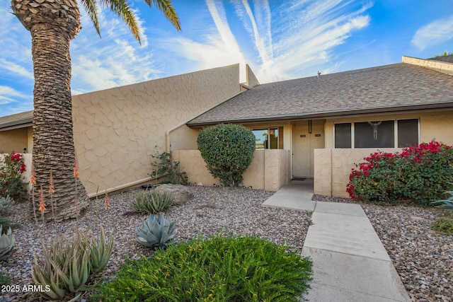 view of front of house with a shingled roof, fence, and stucco siding