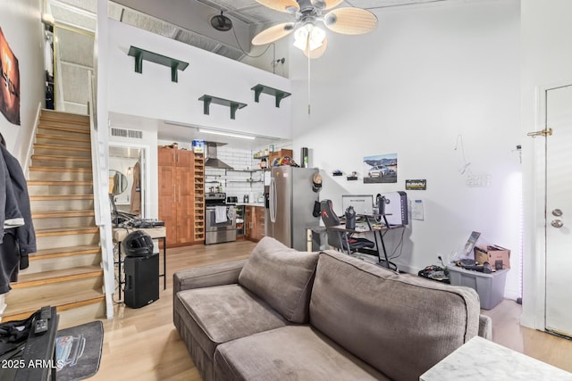 living room with a ceiling fan, light wood-type flooring, visible vents, and stairs