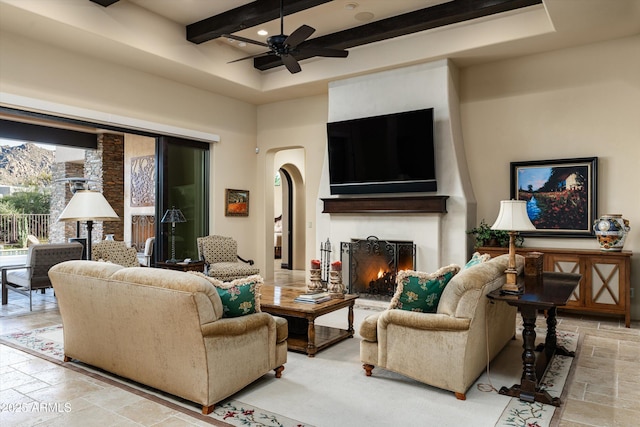 living room with ceiling fan, a large fireplace, beam ceiling, and a towering ceiling