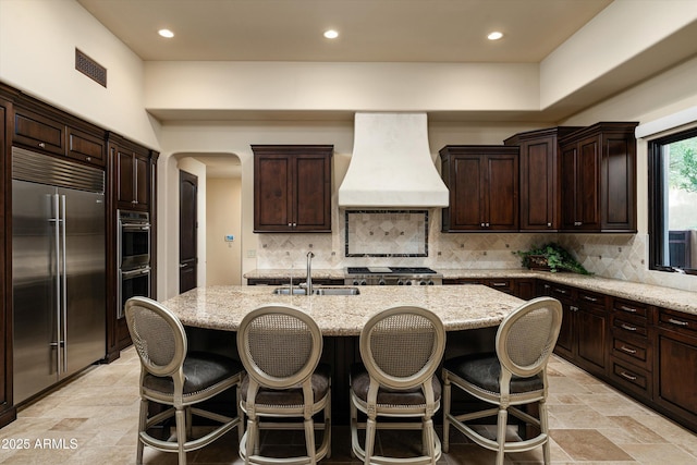 kitchen featuring premium range hood, an island with sink, appliances with stainless steel finishes, and sink