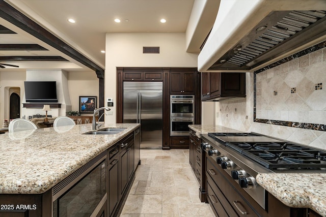 kitchen featuring sink, decorative backsplash, a kitchen island with sink, exhaust hood, and built in appliances