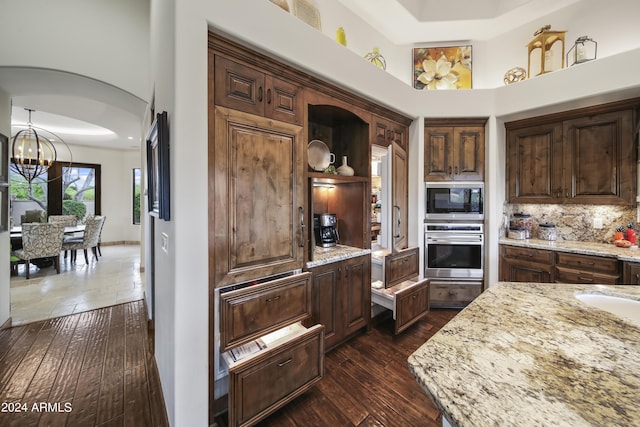 kitchen with built in microwave, stainless steel oven, a chandelier, light stone countertops, and decorative backsplash