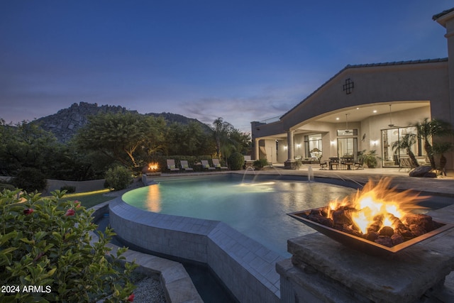 pool at dusk with pool water feature, an outdoor fire pit, and a patio area