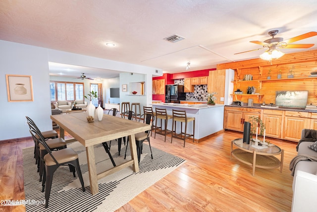 dining space with ceiling fan, wood walls, light wood-type flooring, and a textured ceiling