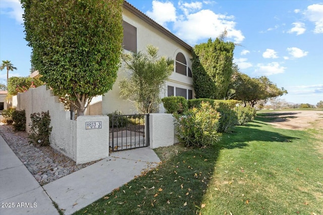 view of side of home with a tile roof, fence, a yard, a gate, and stucco siding