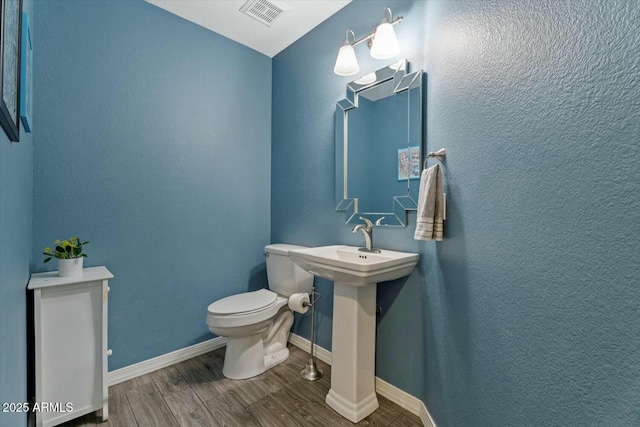 half bath with toilet, wood finished floors, visible vents, and baseboards