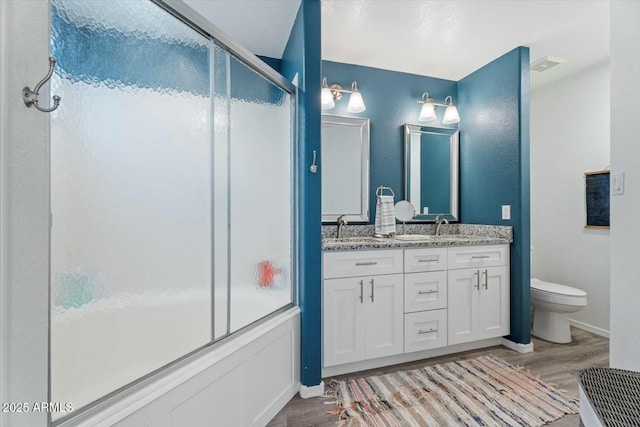 bathroom featuring double vanity, visible vents, toilet, wood finished floors, and a sink