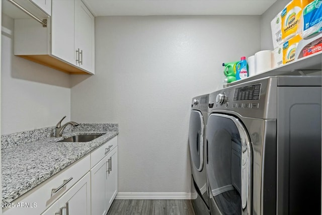 washroom with dark wood-style floors, washing machine and clothes dryer, cabinet space, a sink, and baseboards