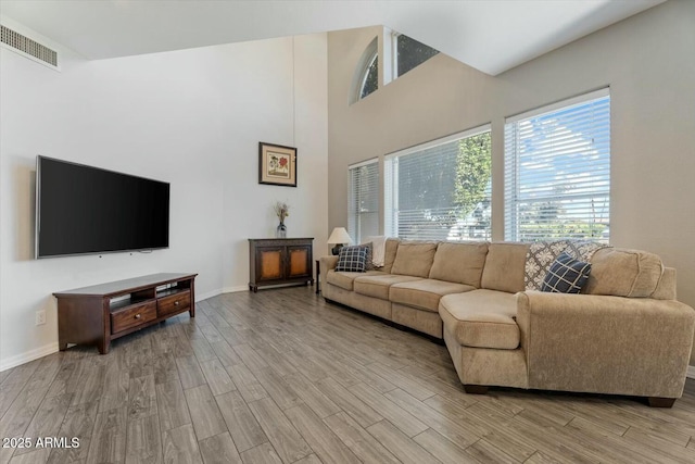 living area with light wood-style floors, baseboards, a high ceiling, and visible vents