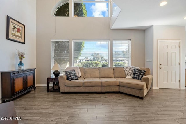 living area with recessed lighting, baseboards, a towering ceiling, and light wood finished floors