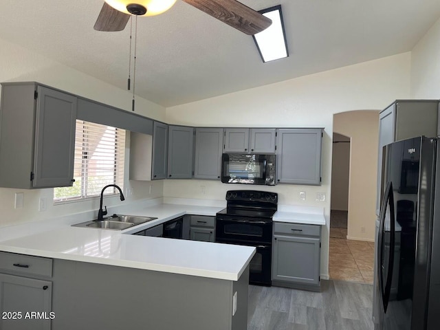 kitchen with lofted ceiling, a peninsula, gray cabinets, light countertops, and black appliances