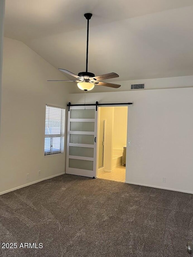 unfurnished bedroom featuring lofted ceiling, a barn door, light colored carpet, a ceiling fan, and visible vents