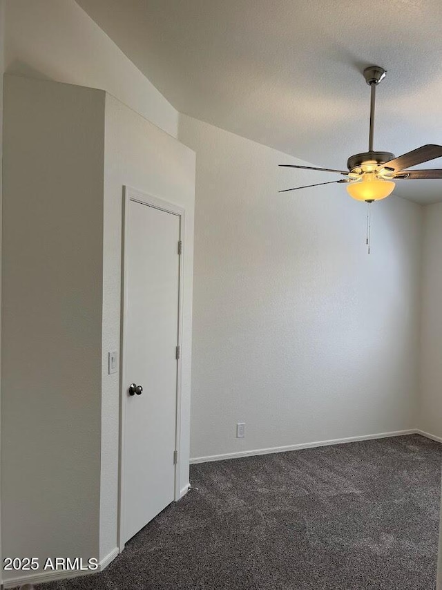 empty room featuring a ceiling fan, dark carpet, and baseboards