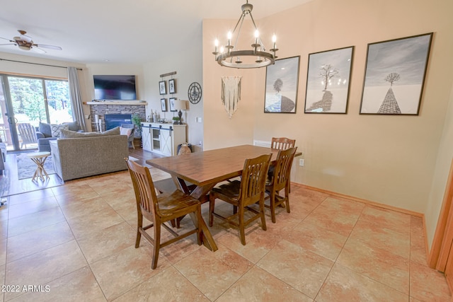 tiled dining room featuring a stone fireplace and ceiling fan with notable chandelier