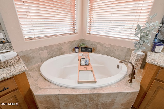 bathroom featuring a wealth of natural light, tiled bath, and vanity