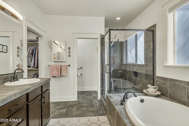 full bath featuring a walk in closet, a bath, a stall shower, vanity, and baseboards