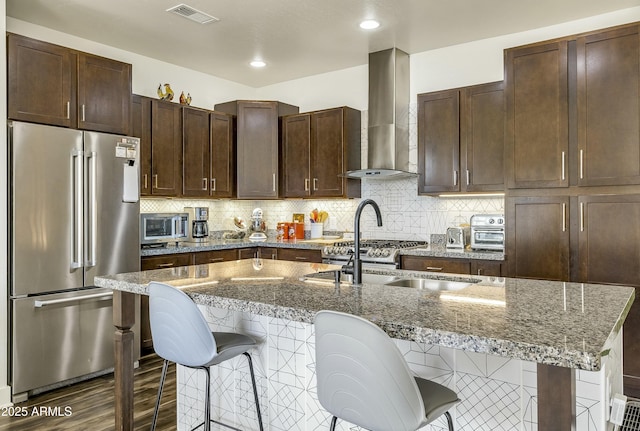 kitchen with visible vents, dark brown cabinetry, a breakfast bar, wall chimney range hood, and high quality fridge