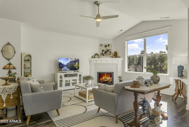 living area featuring a ceiling fan, visible vents, a tiled fireplace, wood finished floors, and lofted ceiling
