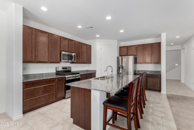 kitchen with visible vents, a kitchen island with sink, a breakfast bar area, a sink, and stainless steel appliances