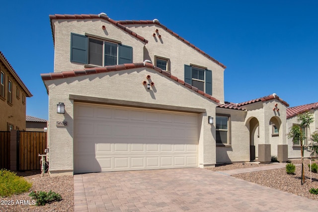 mediterranean / spanish house featuring a tile roof, a garage, decorative driveway, fence, and stucco siding