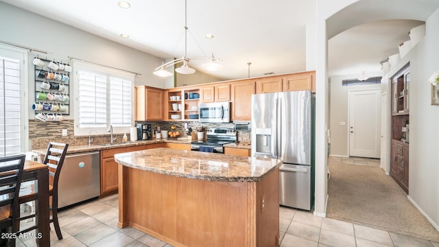 kitchen with sink, light stone counters, appliances with stainless steel finishes, a kitchen island, and pendant lighting