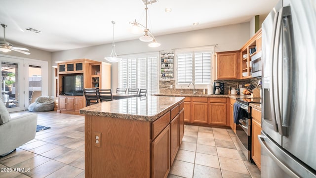 kitchen with stainless steel appliances, a center island, tasteful backsplash, light stone countertops, and decorative light fixtures