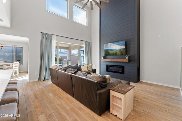 living room featuring a towering ceiling, a fireplace, ceiling fan, and light wood-type flooring