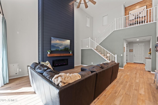 living room with light hardwood / wood-style flooring, a large fireplace, ceiling fan, and a high ceiling