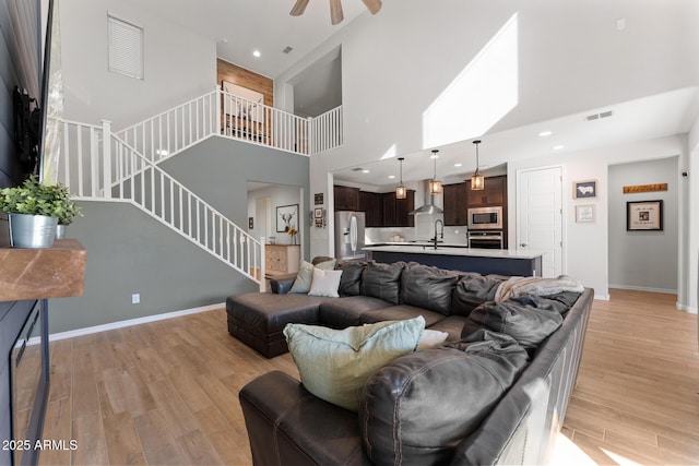 living room featuring ceiling fan, a towering ceiling, sink, and light wood-type flooring