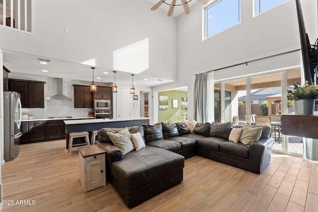 living room featuring light hardwood / wood-style flooring, ceiling fan, and a high ceiling