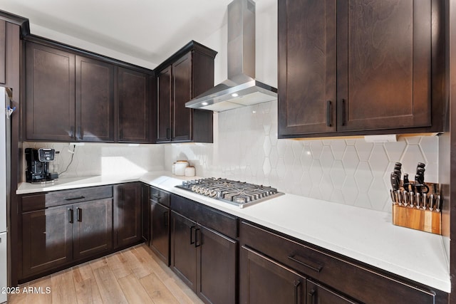 kitchen with tasteful backsplash, stainless steel gas stovetop, light hardwood / wood-style floors, and wall chimney exhaust hood