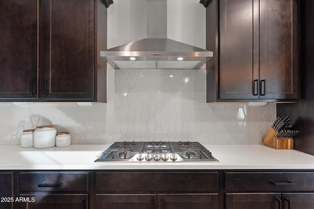 kitchen with backsplash, dark brown cabinetry, stainless steel gas stovetop, and wall chimney range hood