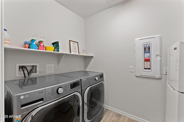 clothes washing area with electric panel, washer and dryer, and light wood-type flooring