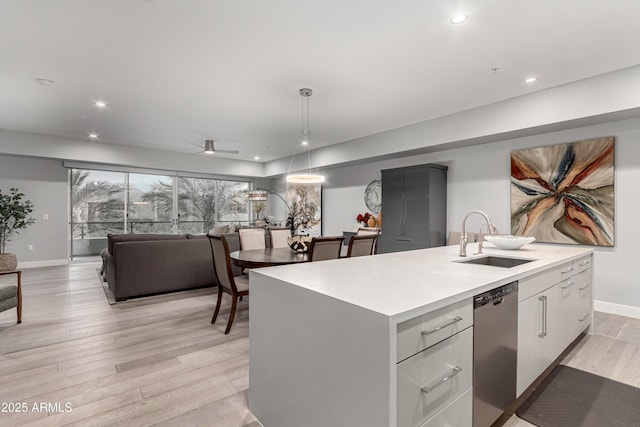 kitchen featuring light wood finished floors, an island with sink, a sink, light countertops, and dishwasher