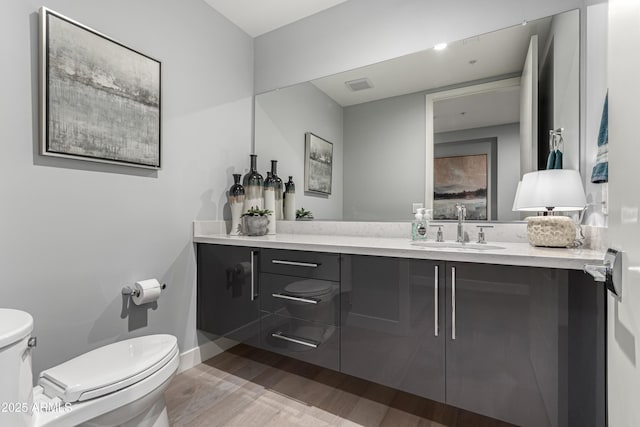 bathroom featuring visible vents, baseboards, toilet, wood finished floors, and vanity